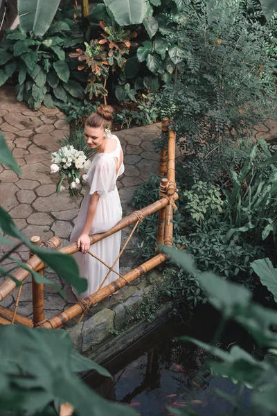 Overhead view of attractive bride posing in white dress with wedding bouquet in tropical garden — Stock Photo