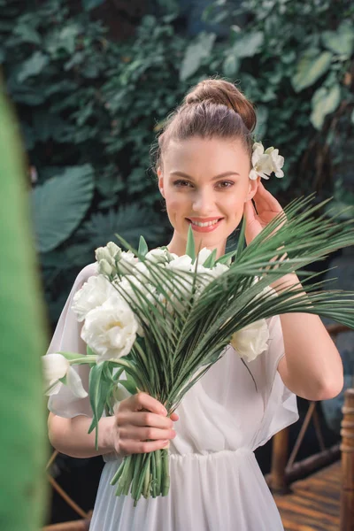 Beautiful smiling bride posing in white dress with wedding bouquet in tropical garden — Stock Photo