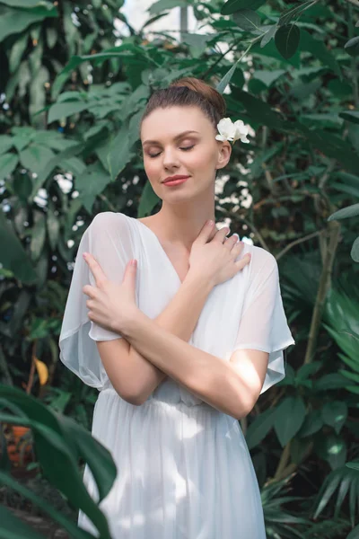 Beautiful bride in white dress with closed eyes posing in tropical garden — Stock Photo