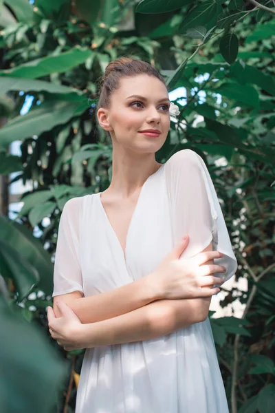 Attractive bride in white dress with crossed arms posing in tropical garden — Stock Photo