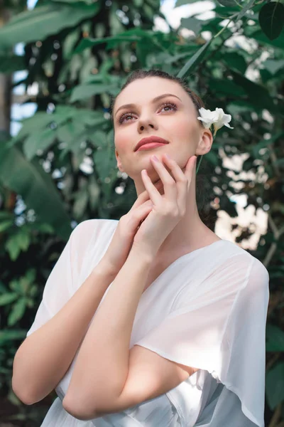 Dreamy girl in white dress with flower in hair posing in tropical garden — Stock Photo