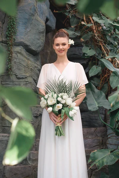 Schöne glückliche Braut posiert im weißen Kleid mit Brautstrauß — Stockfoto