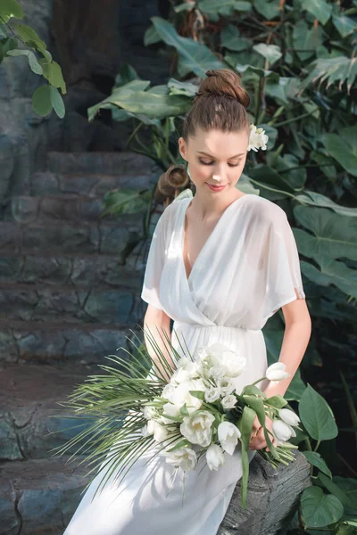 Приваблива наречена позує в білій сукні з весільним букетом — стокове фото