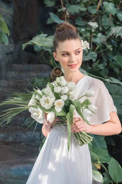 Hermosa novia posando en vestido blanco con ramo de boda - foto de stock