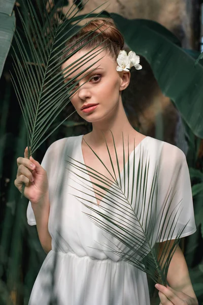 Hermosa chica en vestido de verano blanco posando con hojas de palma tropical - foto de stock