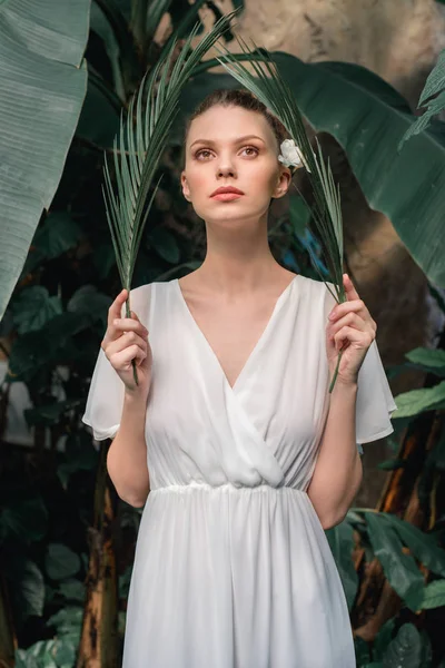 Stylish girl in white summer dress posing with tropical palm leaves — Stock Photo