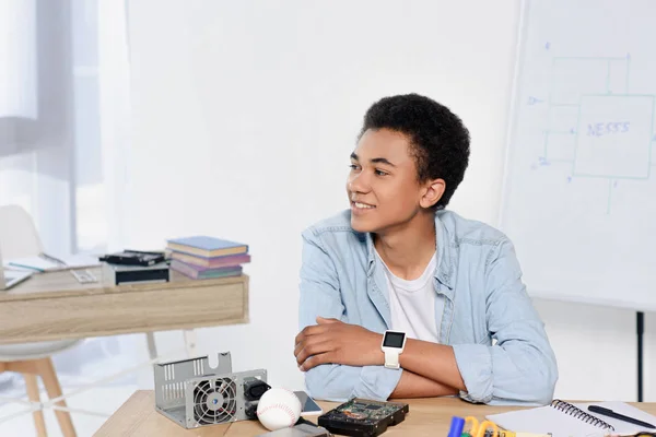 Adolescente afroamericano sentado a la mesa con equipo técnico en casa - foto de stock