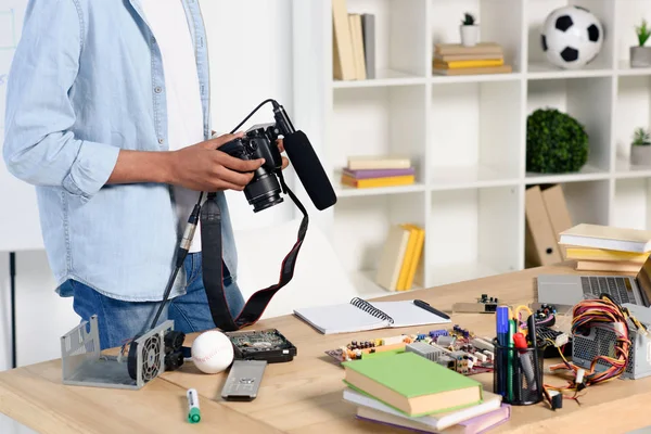 Imagen recortada de adolescente afroamericano sosteniendo cámara digital para disparar vlog en casa - foto de stock