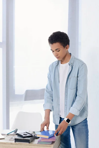 Adolescent afro-américain mettre des livres sur la table à la maison — Photo de stock