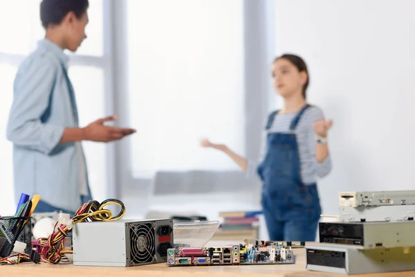 Multicultural friends discussing homework at home with computer motherboard on foreground — Stock Photo