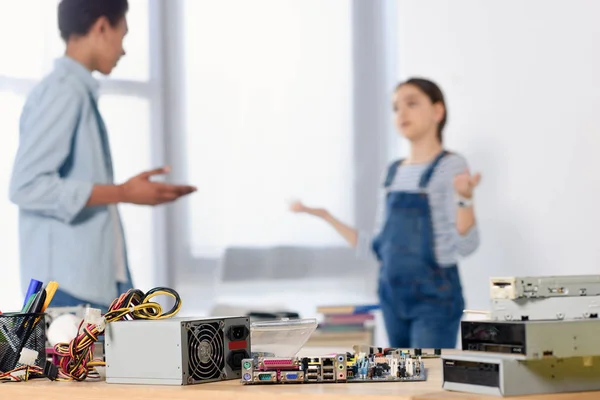 Amigos multiculturais discutindo lição de casa em casa com placa-mãe de computador em primeiro plano — Fotografia de Stock