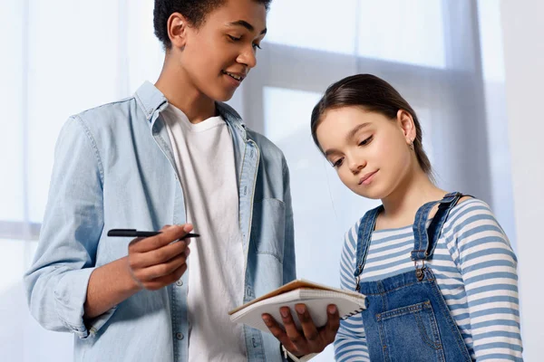 Vista de ángulo bajo de amigos multiculturales mirando el cuaderno en casa - foto de stock