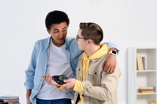 Multicultural teen boys hugging and fixing computer circuit at home — Stock Photo