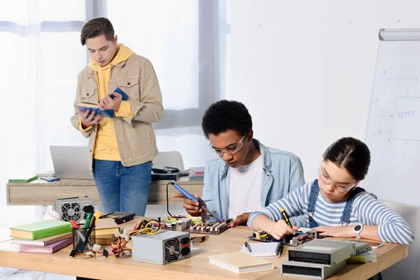 Multicultural teenagers soldering computer circuit and motherboard at home — Stock Photo