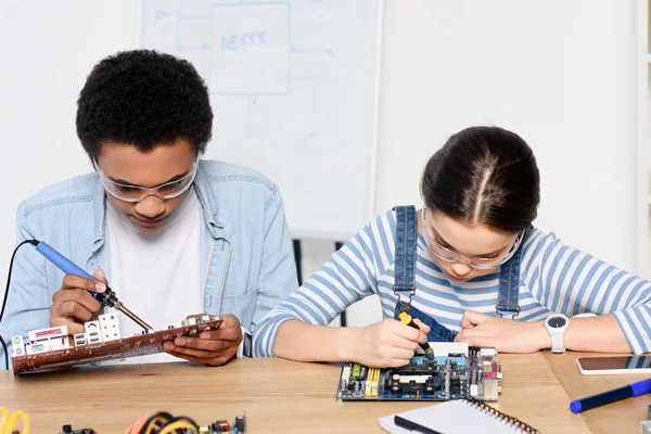 Multicultural friends soldering computer motherboard and fixing circuit at home — Stock Photo