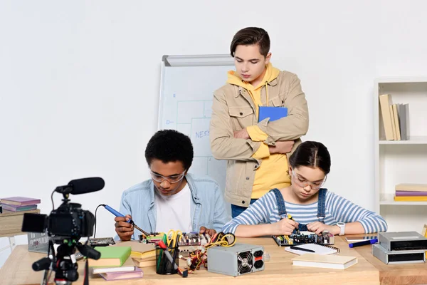 Teenie-Junge beobachtet, wie multikulturelle Freunde zu Hause Computerschaltungen mit Lötkolben löten — Stockfoto