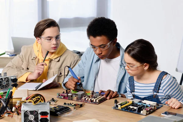 Multicultural teenagers soldering computer circuit with soldering iron at home — Stock Photo