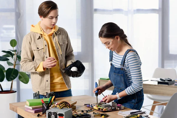 Adolescente chico viendo cómo hembra adolescente soldadura circuito informático con soldador en casa - foto de stock