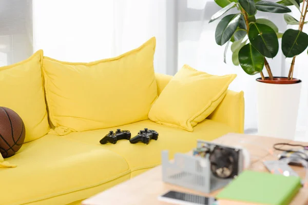 Ігрові автомати та баскетбольний м'яч на жовтому дивані вдома — стокове фото