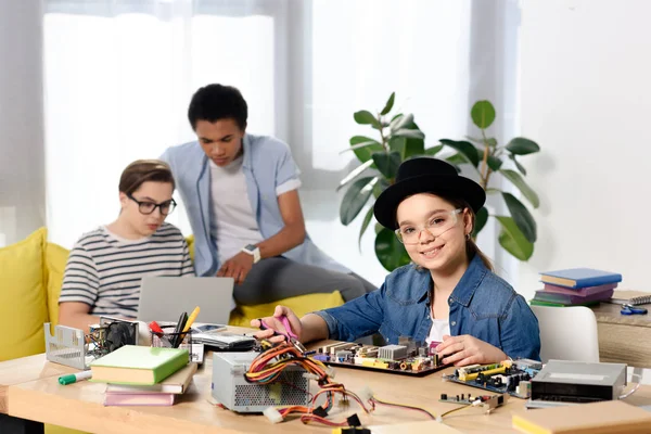 Multicultural teen boys using laptop and female kid fixing computer motherboard at home — Stock Photo