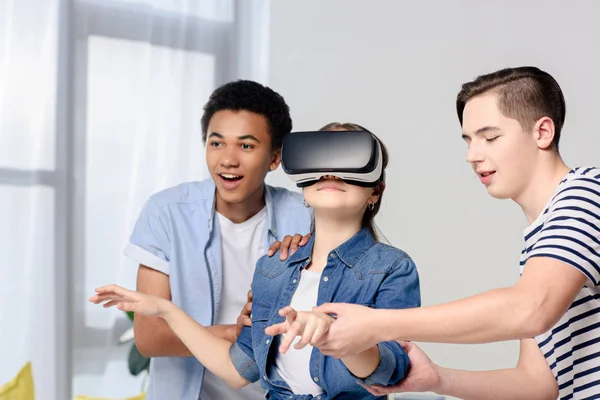 Adolescentes multiculturales apoyando amigo con auriculares de realidad virtual en casa - foto de stock