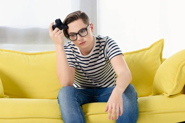 Sad teen boy holding gamepad and sitting on yellow sofa at home — Stock Photo