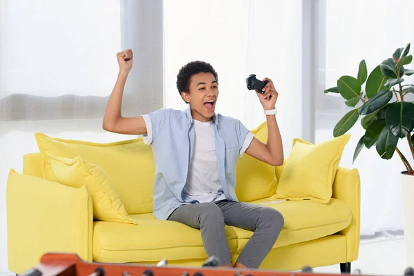 Felice adolescente afro-americano vincente videogioco e mostrando sì gesto a casa — Foto stock