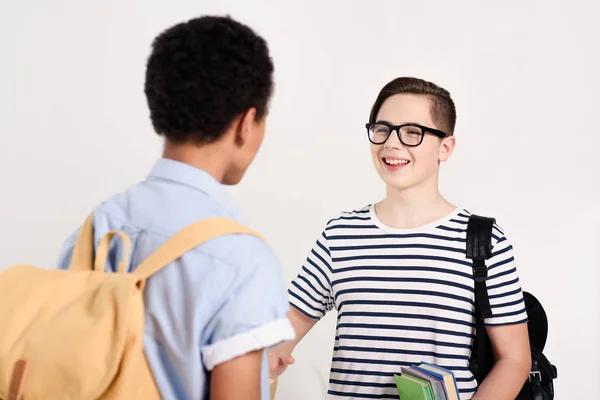 Мультикультурні хлопчики-підлітки з сумками розмовляють ізольовано на білому — стокове фото