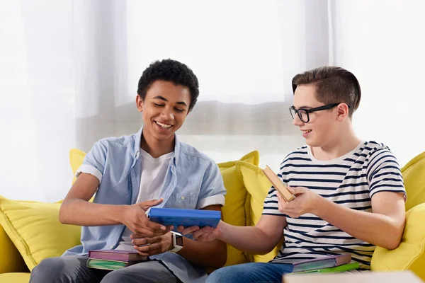 Caucásico adolescente chico pasando libros a africano americano amigo en casa - foto de stock