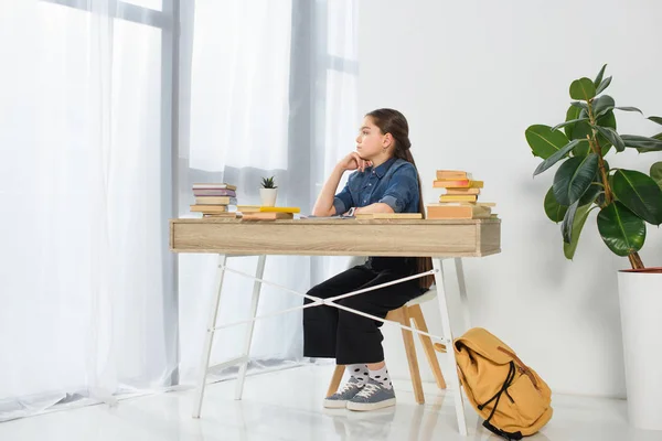 Visão lateral da adorável criança pré-adolescente sentada à mesa em casa — Fotografia de Stock