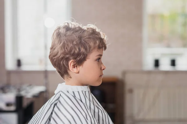 Side view of little kid covered with striped cloth at barbershop — Stock Photo