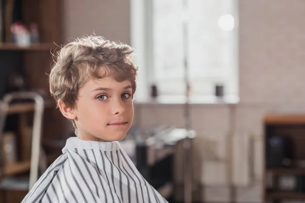 Adorable petit enfant couvert de tissu rayé au salon de coiffure — Photo de stock