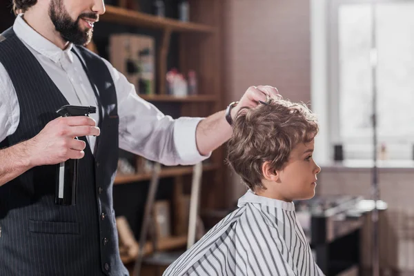 Tiro cortado de barbeiro barbudo pentear e pulverização de cabelo de criança — Fotografia de Stock