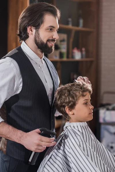 Handsome bearded barber combing hair of little kid — Stock Photo