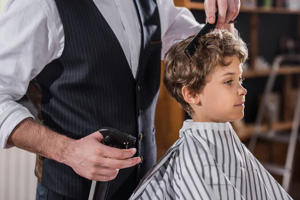 Recortado tiro de peluquero peinando pelo de niño pequeño - foto de stock