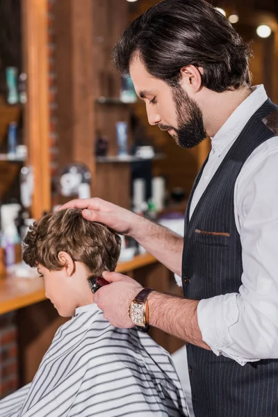 Adorable enfant bouclé se faire couper les cheveux du coiffeur avec tondeuse à cheveux — Photo de stock