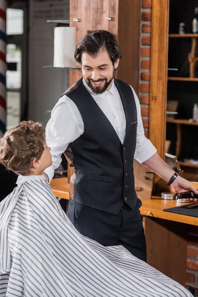 Happy barber with Hair Clipper preparing to cut hair of adorable little kid — Stock Photo