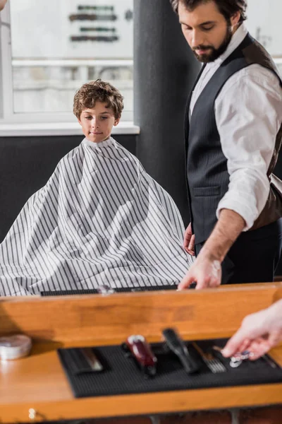 Mirror reflection of barber preparing to cut hair of little kid — Stock Photo