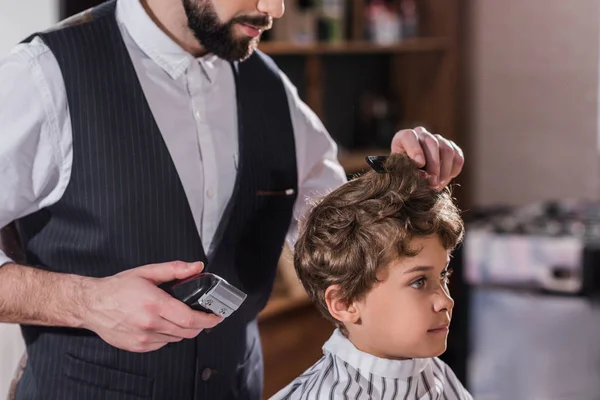 Abgeschnittene Aufnahme eines Friseurs, der Haare eines kleinen Kindes mit Haarschneidemaschine schneidet — Stockfoto