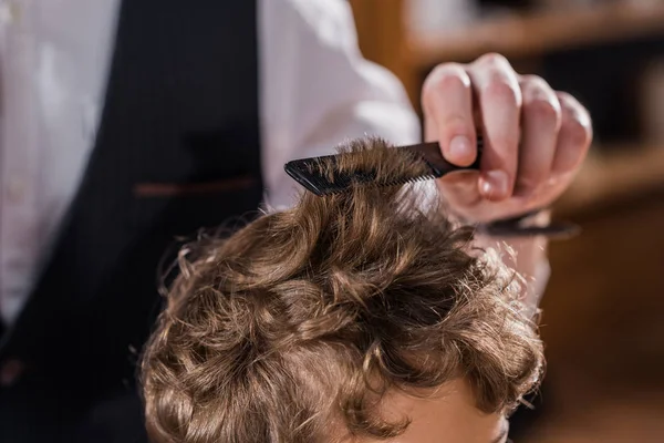 Recortado tiro de peluquero peinando pelo de niño pequeño - foto de stock