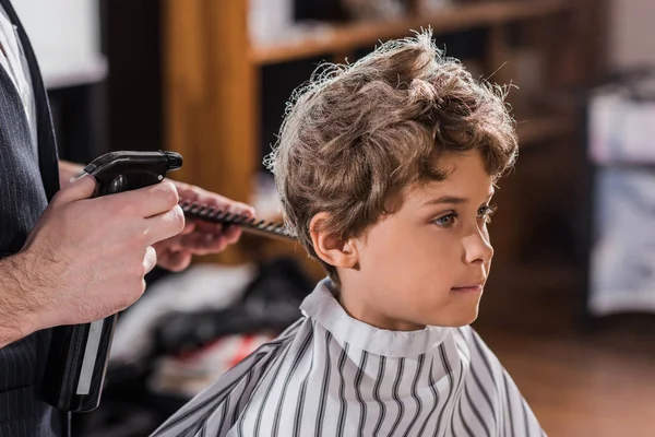 Colpo ritagliato di barbiere che spruzza capelli di bambino adorabile a negozio di barbiere di bambini — Foto stock