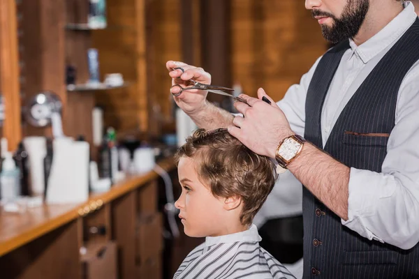 Vista lateral del peluquero cortando pelo de niño rizado - foto de stock