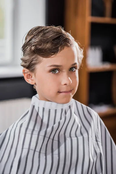 Close-up shot of little kid covered with striped cloth at barbershop — Stock Photo
