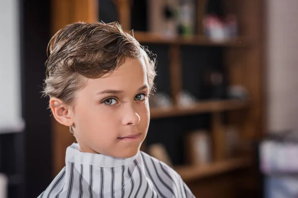 Close-up shot of adorable little kid covered with striped cloth at barbershop — Stock Photo