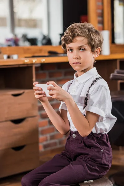 Adorable little kid using smartphone at barbershop — Stock Photo