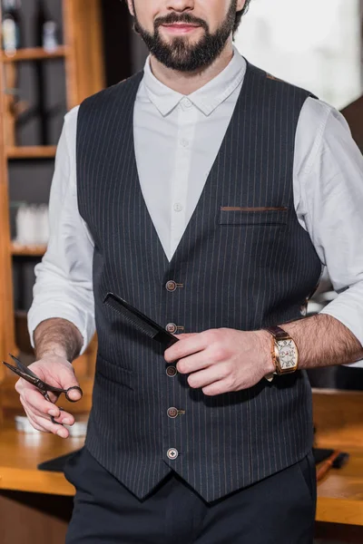 Tiro recortado de barbero guapo con tijeras y peine - foto de stock