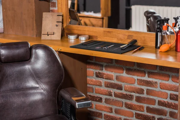 Парикмахерское кресло и инструменты на стойке в парикмахерской — стоковое фото