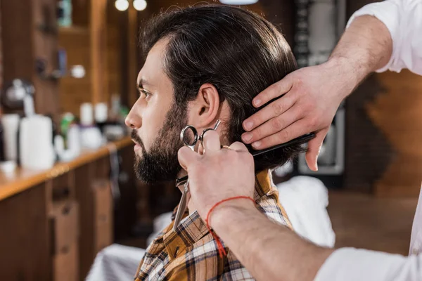 Vista lateral de homem bonito recebendo corte de cabelo na barbearia — Fotografia de Stock