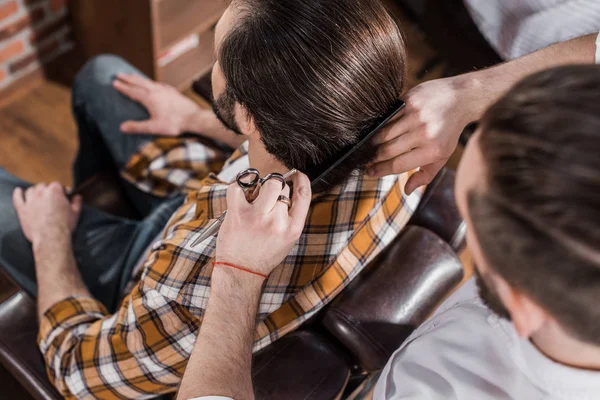 Vista de ángulo alto de peluquería peinando el cabello del cliente en la barbería - foto de stock