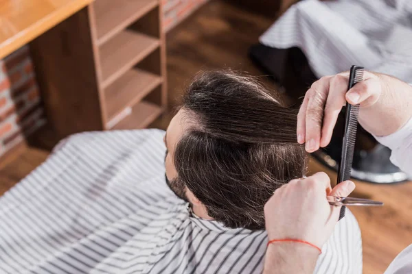 Vista de ángulo alto de peluquero corte de pelo del cliente con tijeras - foto de stock